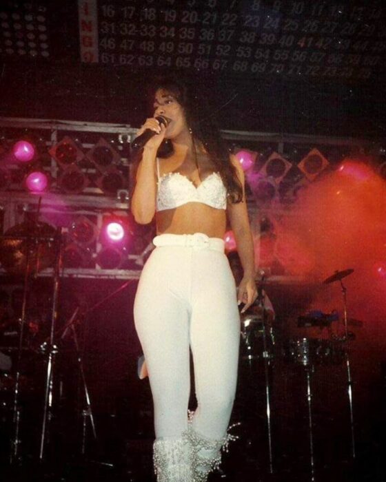 Selena Quintanilla usando un outfit blanco con botas de lentejuelas y bustier blanco