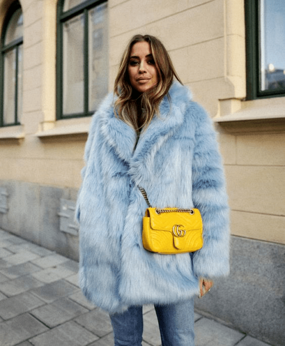 chica de cabello claro usando abrigo afelpado azul celeste, bolso amarillo y jeans