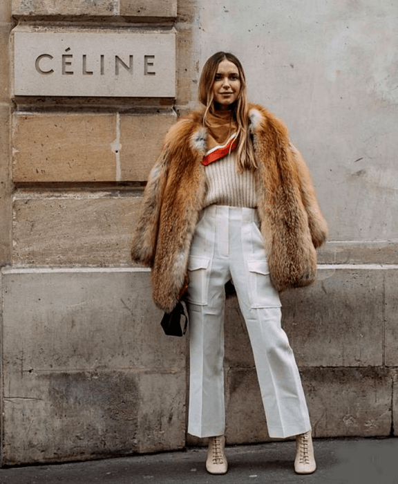 chica rubia utilizando abrigo afelpado beige y café, suéter crema, pantalones de vestir blancos, botines de tacón blancos con agujetas y mascada mostaza