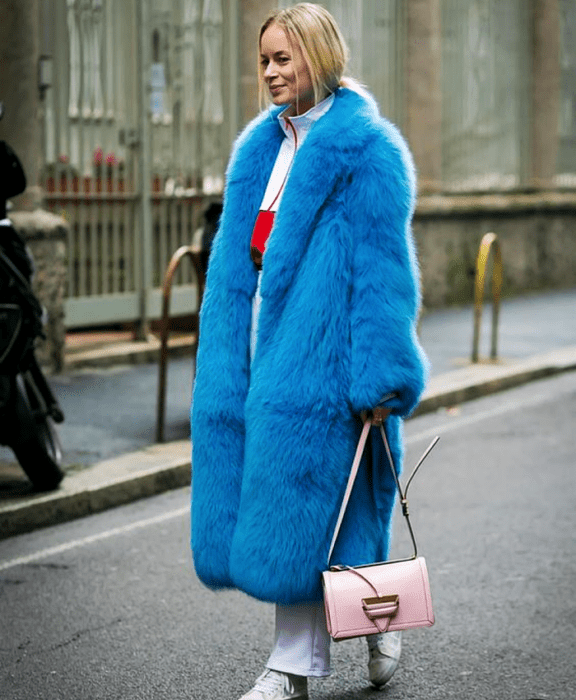 chica rubia con sudadera blanca y detalles rojos, abrigo afelpado azul brillante, pantalones blancos, tenis blancos y bolso rosa pastel