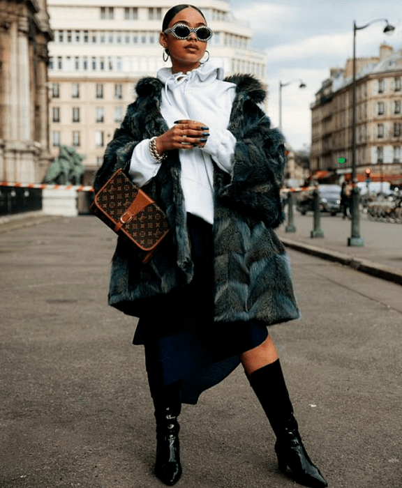 chica morena usando lentes de sol, sudadera blanca, abrigo afelpado azul con vetas negras, falda midi azul marino, botas largas negras de cuero y bolso café LV