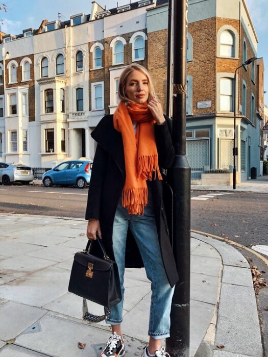 Chica usando bufanda larga de color naranja, jeans y abrigo negro
