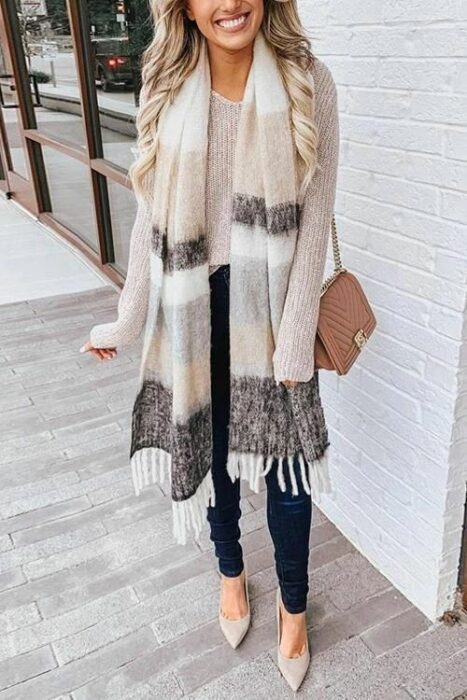 Chica usando bufanda larga de color beige, con líneas cafés y grises, suéter beige y jeans negros