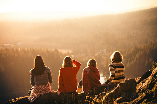 Chicas sentadas en la orilla de una colina mirando el atardecer