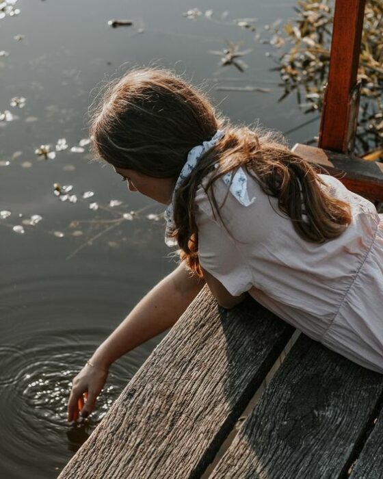 Chica tocando el agua de un lago con la mano