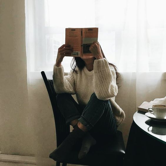 Chica con suéter blanco leyendo un libro