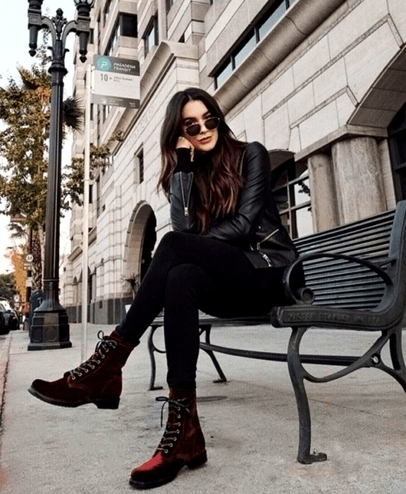 mujer de cabello castaño con lentes de sol, suéter negro de manga larga, chaqueta de cuero negro, botines rojos de terciopelo y bolso negro