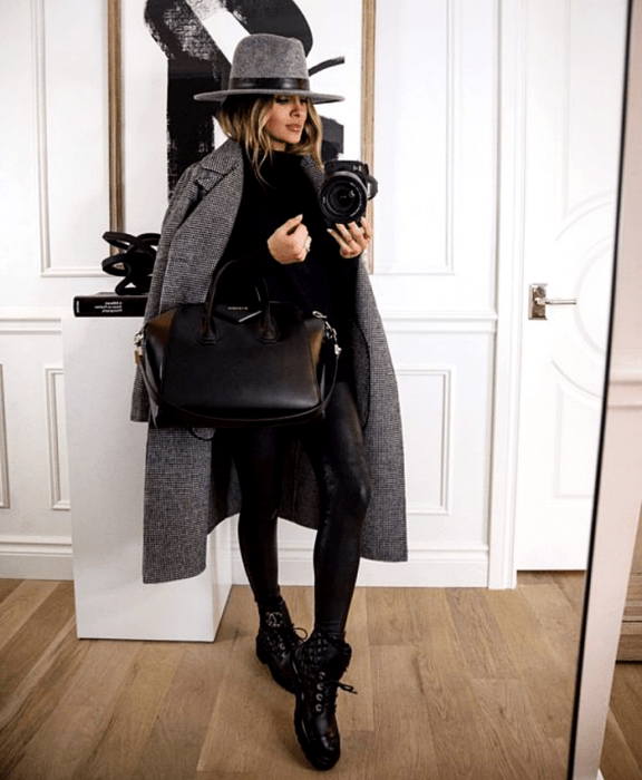 mujer rubia con un sombrero gris, suéter negro, abrigo largo gris, leggings de cuero negro, botines negros sin tacón y bolso grande shopper negro