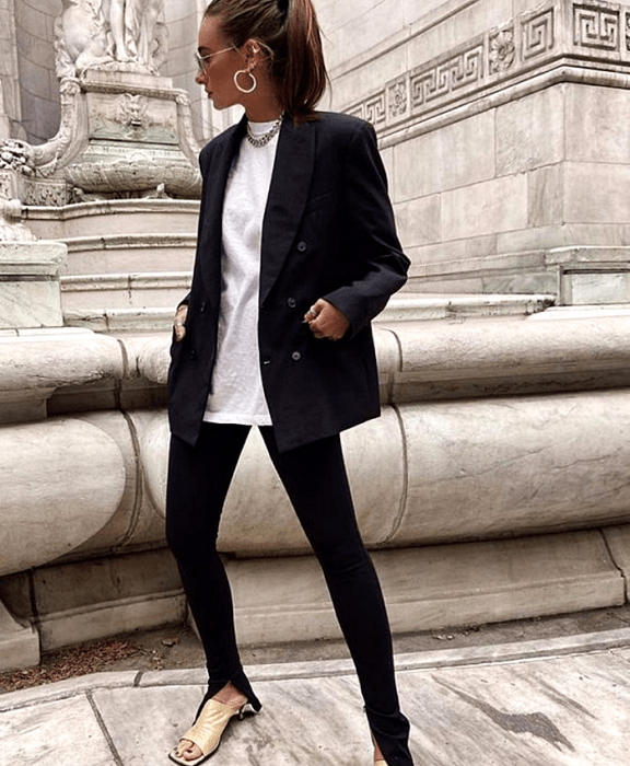 mujer de cabello castaño con lentes de sol, camiseta blanca, blazer azul marino, leggings negros con abertura en el tobillo y sandalias de tacón amarillo pastel
