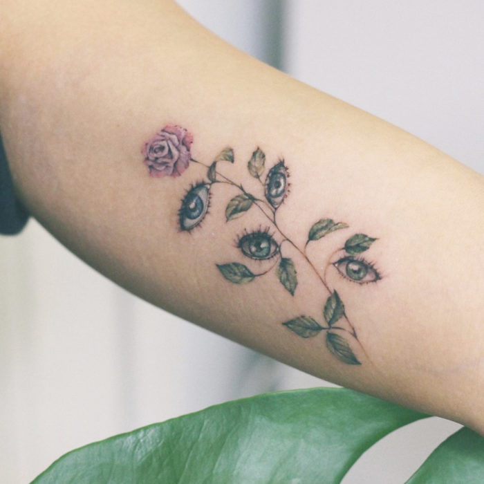 Tatuaje mini, pequeño de flores femeninas rosa con ojos en lugar de hojas, en el brazo