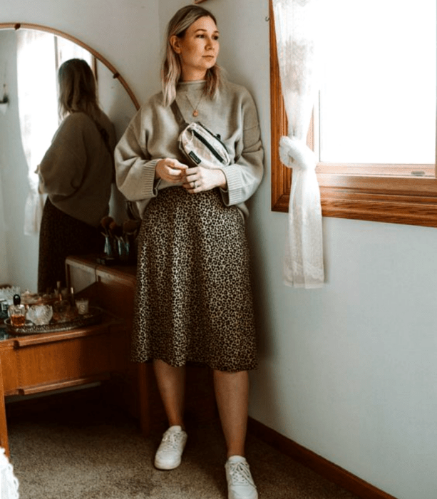 chica rubia curvy usando un suéter beige, falda midi de animal print y tenis blancos