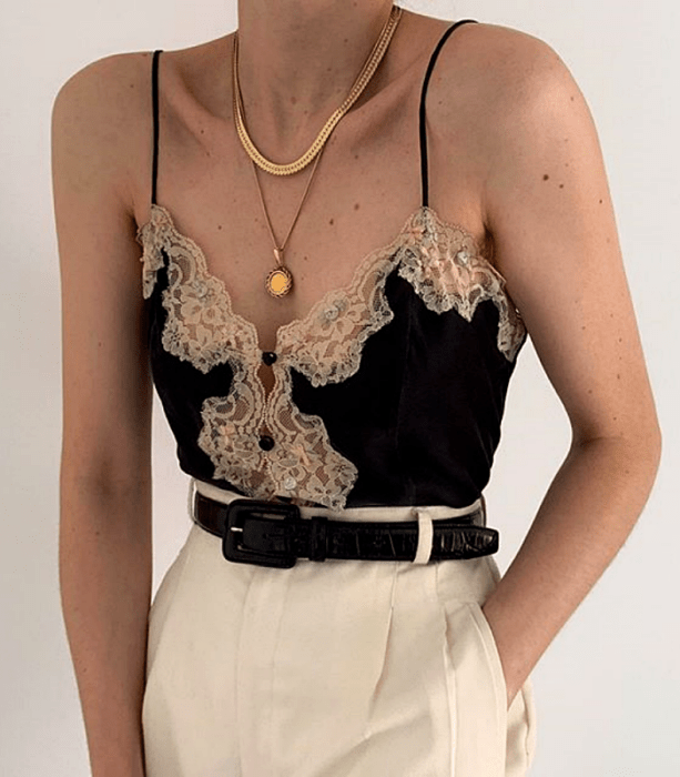 blusa negra de tirantes con encaje beige y botones al frente, cinturón negro de piel, pantalón de vestir blanco a la cintura y collares de oro