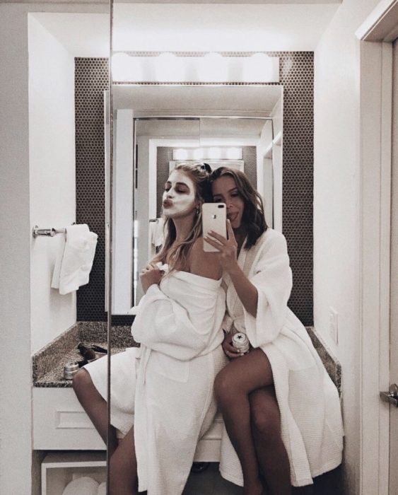 Chicas dentro de un baño tomando una selfie sentadas sobre el lavamanos 