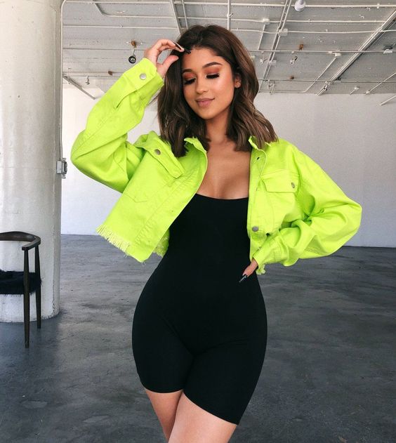 Chica morena de cabello corto con vestido negro y chamarra verde neón