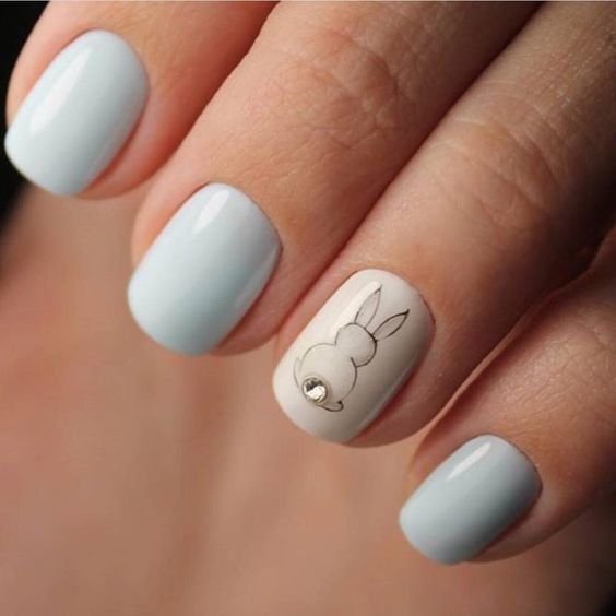 Manicura en tonos azules con una uña en gris claro y la silueta de un conejito