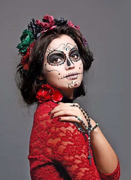 Maquillaje de catrina en rostro completo en tonos blanco y negro y cabello recogido con listones rojos y verdes