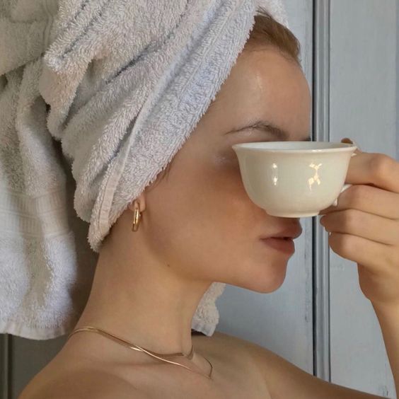 Chica con una toalla en la cabeza se tapa la cara con una taza