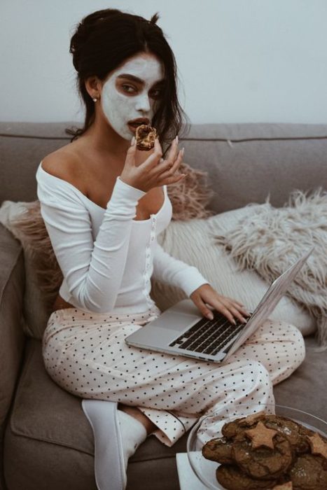 Chica sentada en el sillón con su laptop en las piernas usa una mascarilla de arcilla