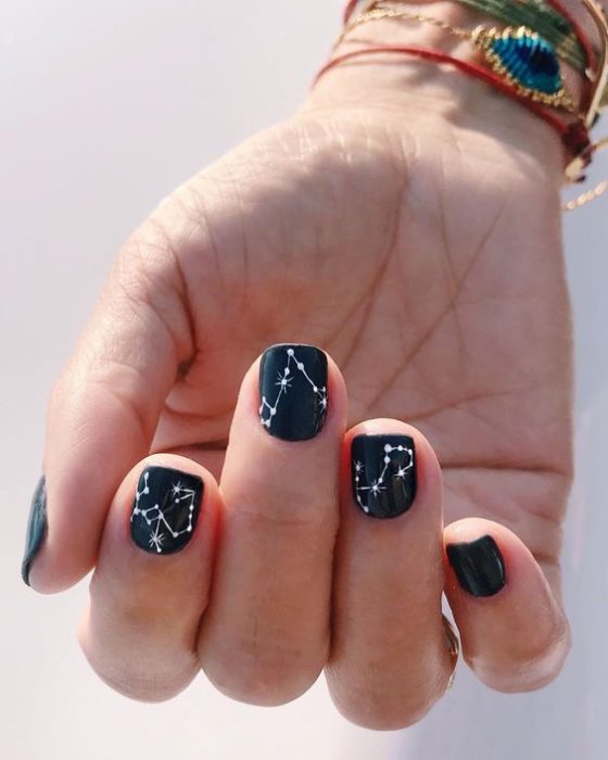 Diseño de manicura en uñas cortas en color negro con constelaciones blancas