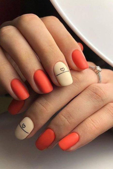 Diseño de manicura en uñas cortas en color rojo con una uña en color beige y detalle negro en efecto mate