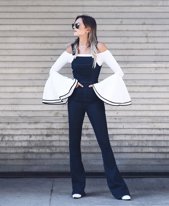 Chica delgada de cabello suelto con overol de mezclilla y blusa blanca con mangas amplias