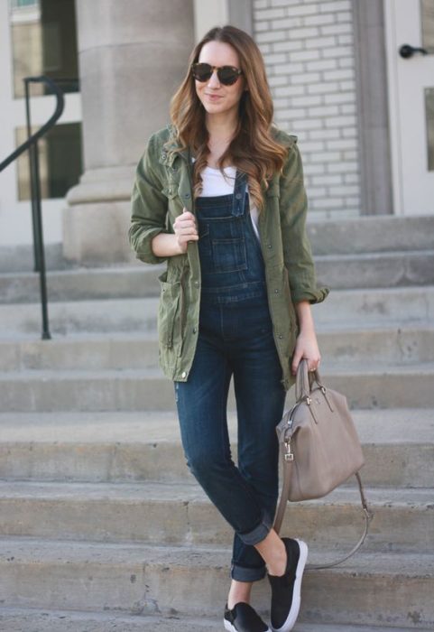 Chica de cabello largo castaño con blusa blanca, overol y chamarra larga verde militar