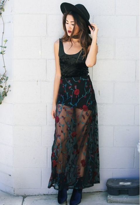 Chica llevando falda con transparencias en negro con bordado de rosas en tono rojo y blusa negra de tirantes con sombrero a juego