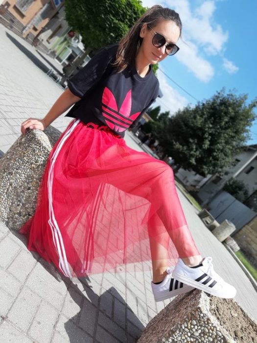 Chica llevando falda con transparencia en color rojo y camisa negra de adidas
