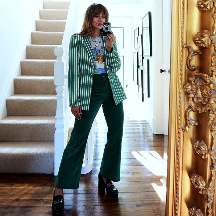 chica de cabello claro usando una camisa blanca estampada con saco verde de rayas blancas, pantalones acampanados verdes y zapatos de tacón negro