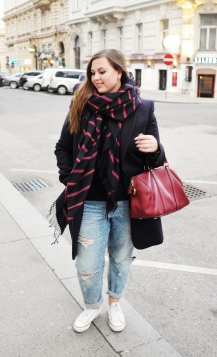 Chica curvy con saco negro, bufanda negra con rayas rojas, jeans claros y converse blancos