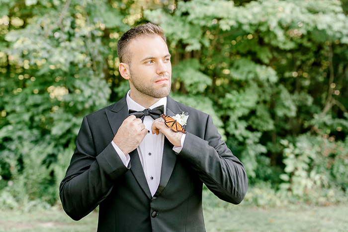 Novio posando para su sesión de fotos de boda mientras una mariposa se posa en su mano