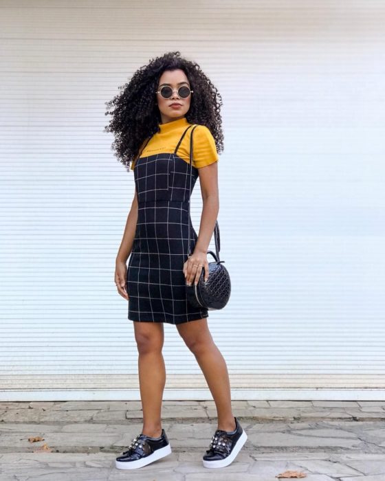 Vestido corto de color negro con estampado de cuadros en líneas blancas y blusa amarilla debajo y tenis negros