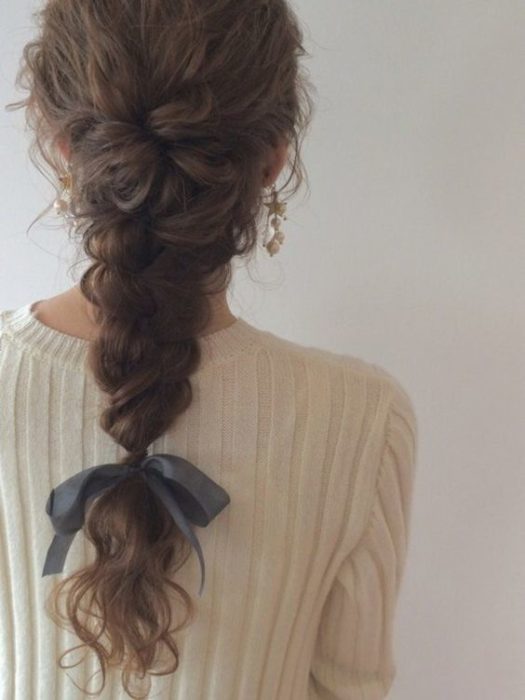 Chica con cabello ondulado, en trenza completa con moño de listón al final