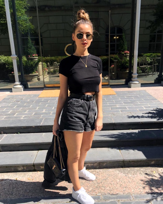 Looks con short vintage; chica con peinado de chongo alto, crop top negro, tenis blancos, lentes de sol