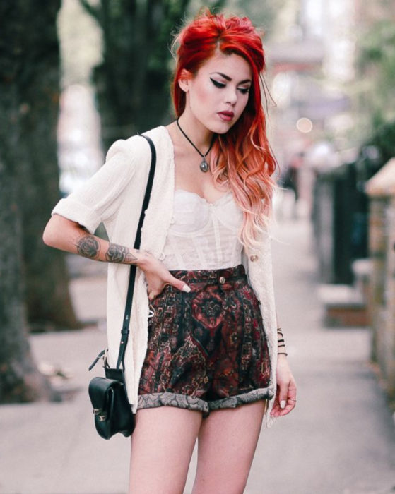 Looks con short vintage; chica rockera pelirroja con tatuajes de flores en los brazos, corsé blanco y short con estampado retro, suéter tejido y bolsa negra