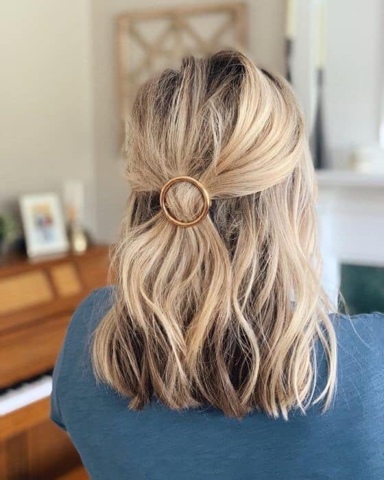 Chica rubia con medio recogido en la cabeza y broche dorado redondo
