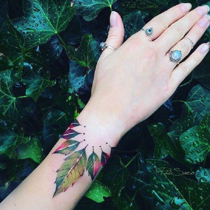 Tatuaje sobre la muñeca de unas hojas de árbol que van cambiando de color de una a otra
