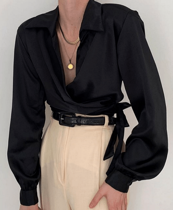 Chica con blusa de satén negro, cinturón negro y pantalones blancos