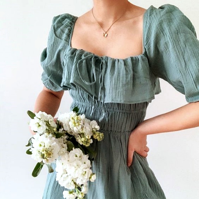mujer usando un vestido verde opaco gris con escote cuadrado y mangas de 3/4, sosteniendo flores blancas