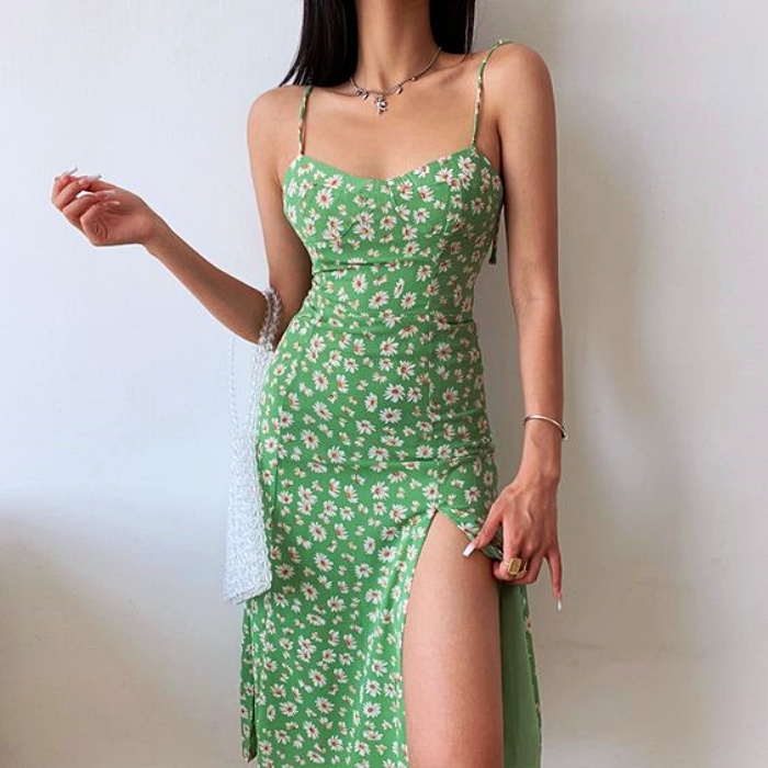 mujer con cabello castaño usando un vestido verde de tirantes con abertura en la pierna y bolso de mano blanco