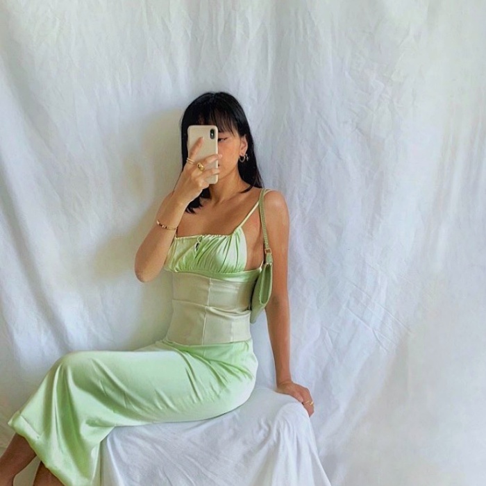 mujer de cabello castaño usando un vestido de satén verde pastel con corset blanco