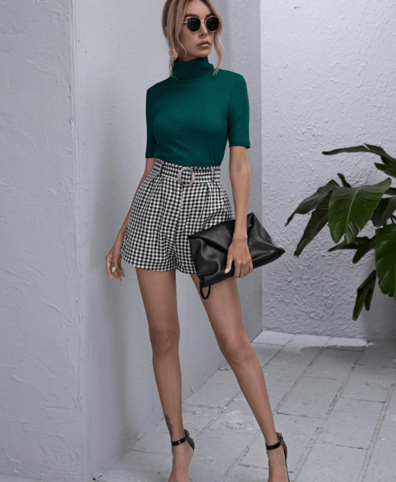 mujer rubia usando gafas de sol, top verde con cuello alto, paperbag shorts de cuadros blancos y negros y zapatos de tacón