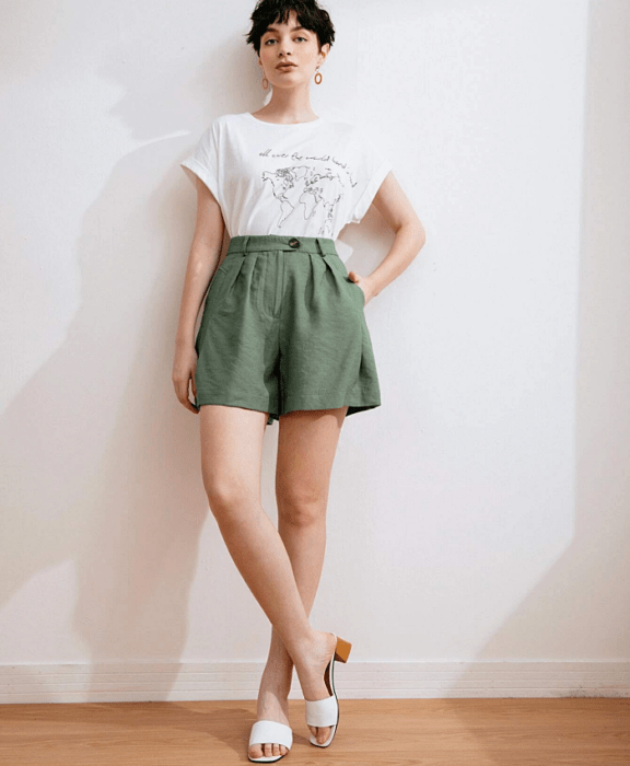 mujer de cabello corto negro con una camiseta blanca de manga corta, paperbag shorts verdes y sandalias blancas