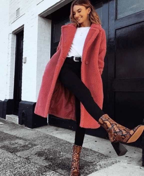 chica de cabello castaño claro usando camiseta blanca, abrigo rosa tipo teddy coat, skinny jeans negros, botines de animal print de cuero
