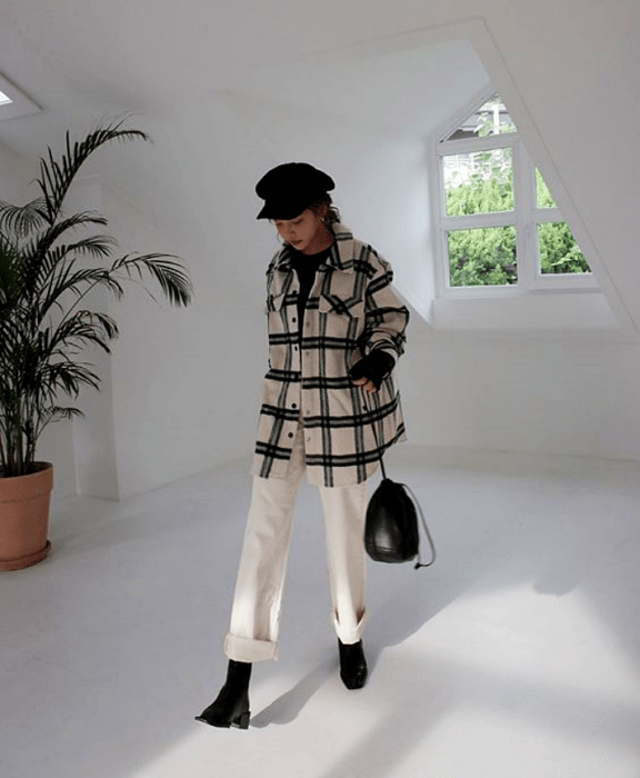 chica usando sombrero negro, abrigo blanco con líneas negras, pantalón blanco, botines negros y bolso negro