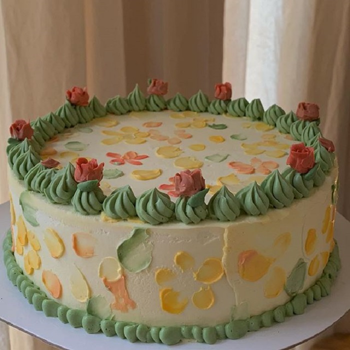 Pastel de la repostera Koike, de fondo blanco, con detalles color amarillos, verdes y flores
