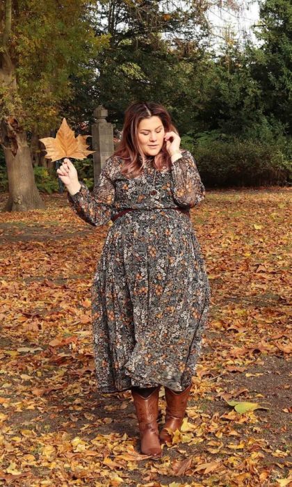 Chica plus size con vestido de chifón largo de flores posando en hojas amarillas