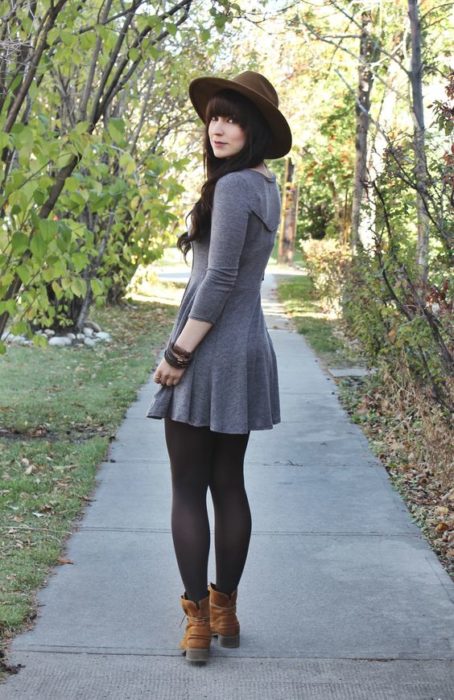 Chica delgada de cabello largo y oscuro con vestido gris, medias negras y sombrero