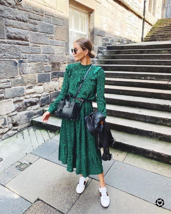 Chica rubia con cabello recogido en un moño bajo, vistiendo vestido verde largo y tenis blancos
