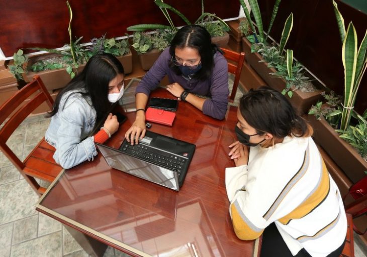 Chicas sentadas en sillas y con laptop tomando clases en línea